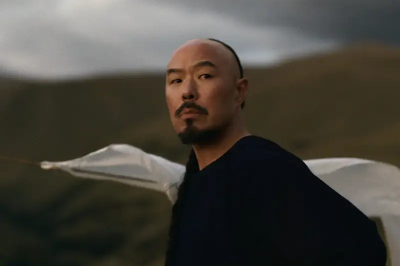 Hoon Lee as Lee in East of Eden, in a dark shirt against rolling hills, a white sheet billowing behind him