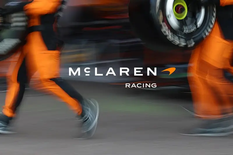 The new McLaren Racing lockup in white over a motion-blurred pit stop, the crew in papaya overalls lifting a tyre