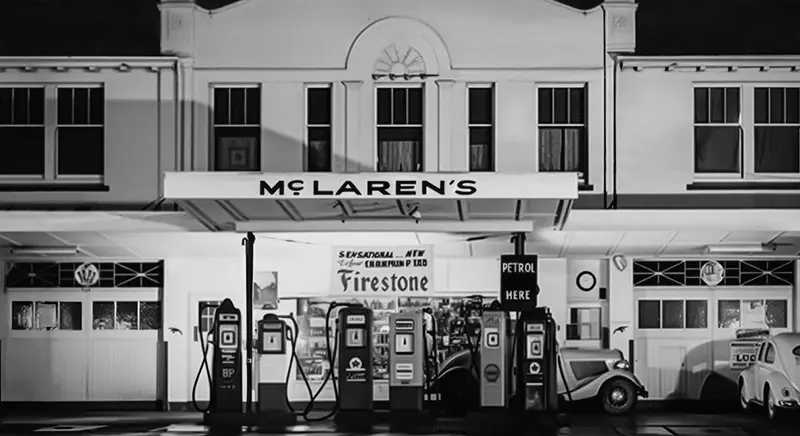 The McLaren family service station at night in black and white, the McLaren’s sign lit above a row of petrol pumps