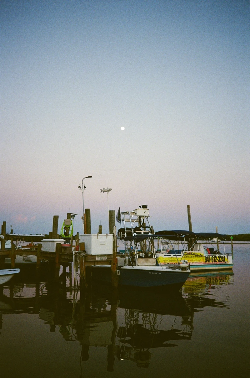 Small fishing boats tied up at a wooden dock at dusk, the water flat and the sky fading from blue to pink.
