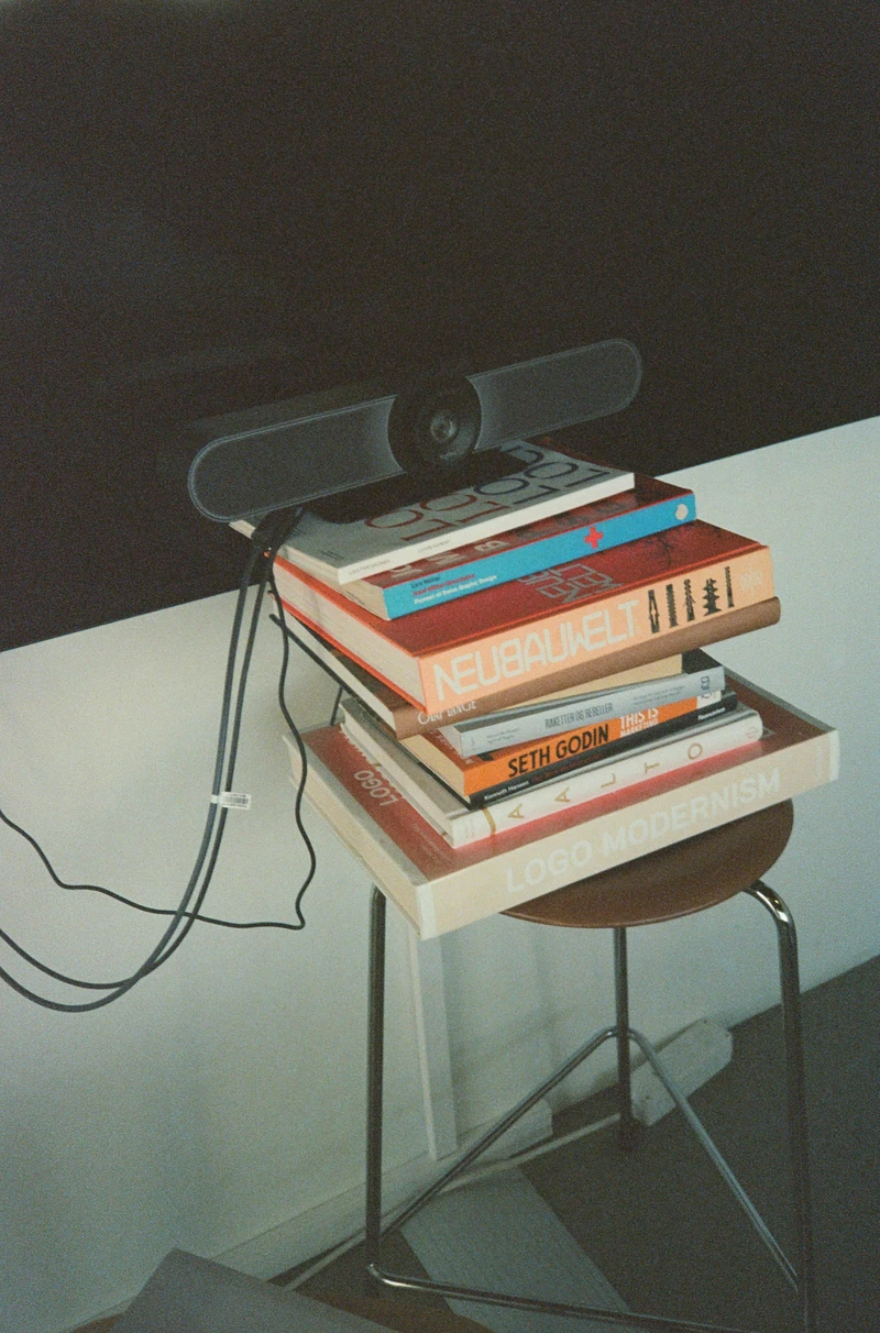 A webcam balanced on a stack of design books on a stool, cables trailing to the floor.