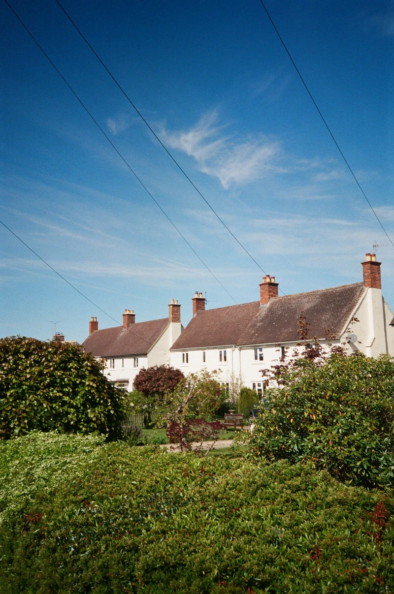 White cottages with brick chimneys behind a hedge, power lines cutting across a deep blue sky.