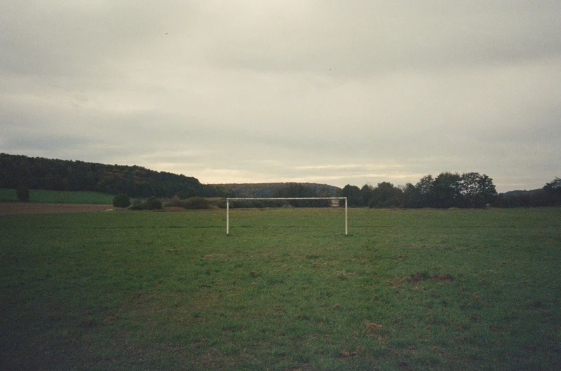 An empty grass pitch under a grey sky, a single goal standing at the far end.