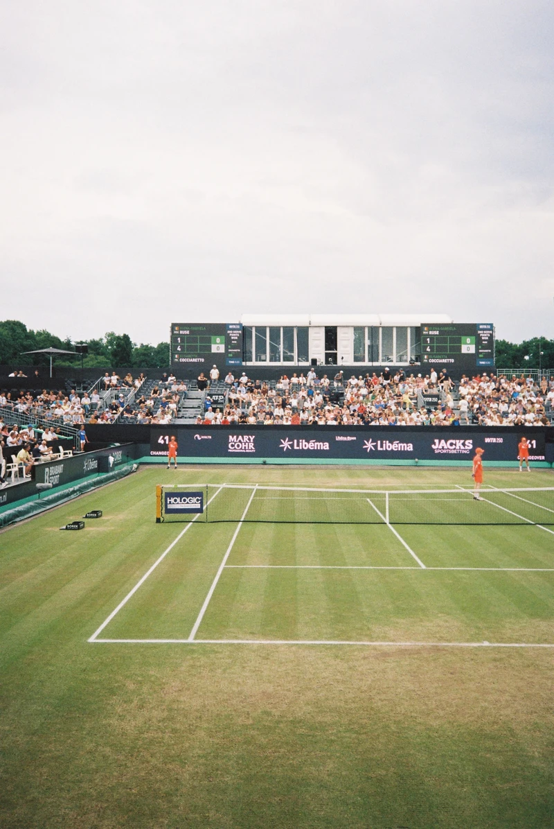 An empty grass tennis court at the Libéma Open, crowd and scoreboard behind.