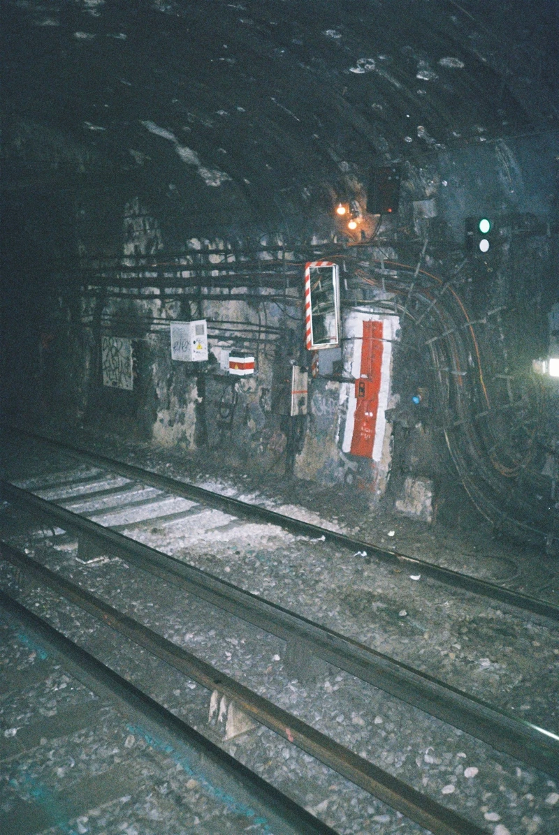 A dim métro tunnel: tracks curving past a soot-black wall hung with a red-and-white marker and a mirror.