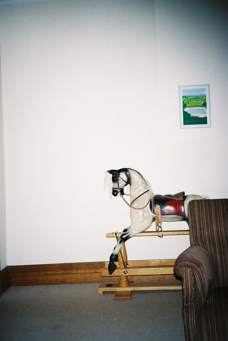 A dappled grey rocking horse against a bare white wall, half hidden behind the arm of a striped sofa.